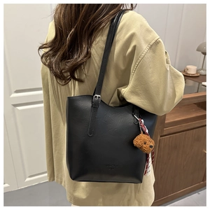 Dettaglio di borsa tote in pelle nera con ciondolo a forma di orso e tracolla regolabile