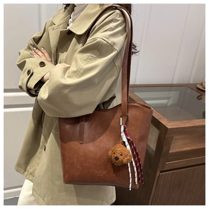 Dettaglio borsa tote in pelle marrone vintage con orsetto di peluche e cinturino intrecciato