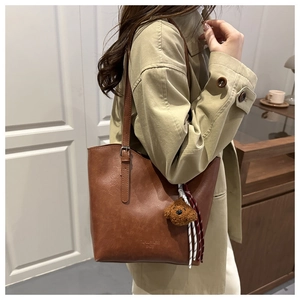 Dettaglio della borsa tote in pelle marrone con ciondolo orsetto e nappina intrecciata