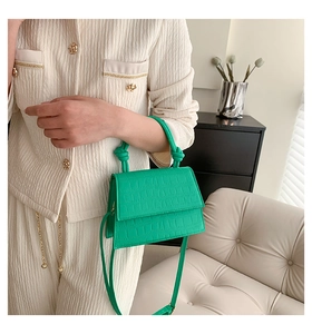 Sac à main vert émeraude à motif crocodile avec poignée nouée posé sur un canapé