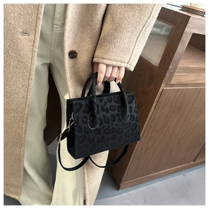 Detail of leopard print crossbody bag held by a model wearing a beige wool coat