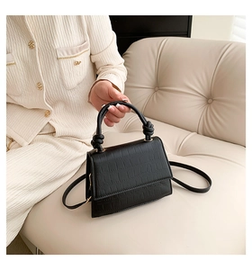 Détail d'un sac noir texture crocodile avec poignée nouée et fine bandoulière élégante