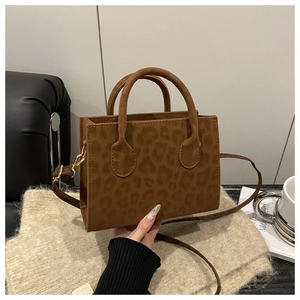 Detail of leopard print crossbody bag with gold hardware on a beige textured blanket