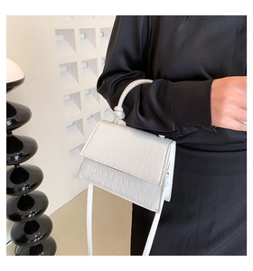 Gros plan d'un sac à main blanc motif crocodile avec poignée nouée et fini texturé