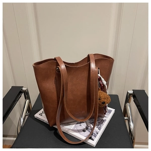Dettaglio borsa tote in pelle marrone con ciondolo a forma di orso su sedia nera