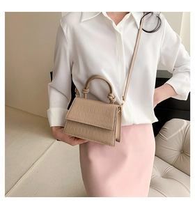 Détail d'un sac beige texture crocodile avec poignée à nœud porté par un mannequin