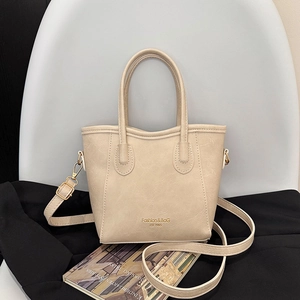 Elegant beige bucket bag with top handles and adjustable strap on white chair