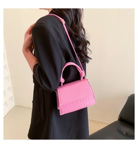 Sac rose en cuir croco avec poignée nouée porté sur un blazer noir chic