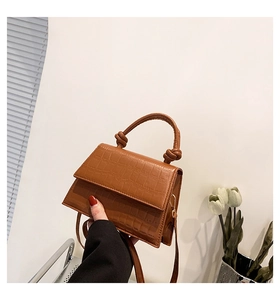 Détail de la texture cuir crocodile marron et poignée nouée sur un sac à bandoulière