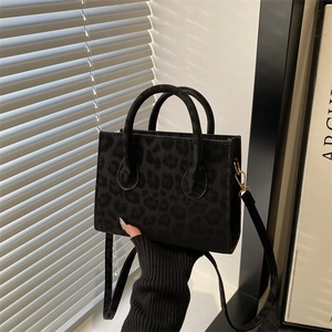 Black leopard print crossbody bag with gold hardware and top handles shown in natural light