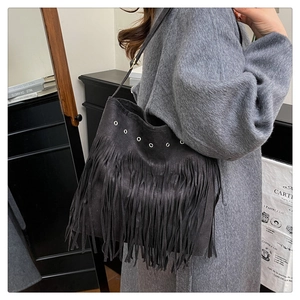 Détail du sac à bandoulière en suède noir avec œillets métalliques et longues franges