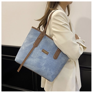 Détail du grand sac cabas en denim bleu avec garniture en cuir marron et étiquette mode