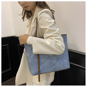 Détail du sac cabas en denim bleu avec lanières en cuir marron et blazer blanc