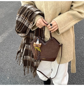 Nahaufnahme braune Beuteltasche mit Steppnaht und einem süßen Bärenanhänger-Accessoire