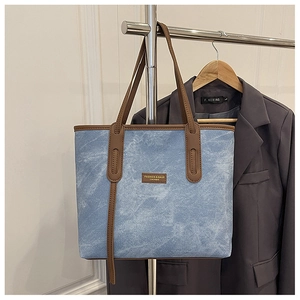 Détail du grand sac cabas en denim bleu avec finitions en cuir marron et étiquette