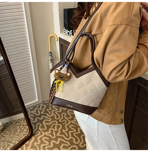 Detail einer beige gesteppten Tragetasche mit braunem Rand und Teddybär-Anhänger