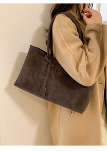 Close-up of a large dark brown suede tote bag with long handles and decorative pendant