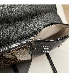 Detail of smooth metal zipper and textured snake skin pattern on black handbag