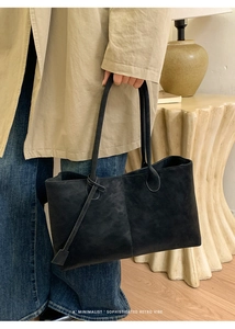 Detail of a minimalist black tote bag with long leather handles in a retro home setting