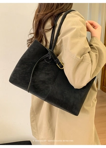 Close-up of a large black suede tote bag with metal buckle detail and minimalist design
