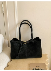 Close-up of black suede tote bag with minimalist strap detail on wooden furniture
