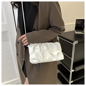 Close-up of a white pleated cloud bag worn as a shoulder bag with a brown blazer