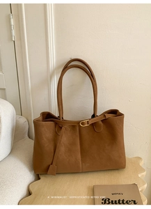 Close-up of caramel leather tote bag featuring vertical stitching and a gold buckle detail