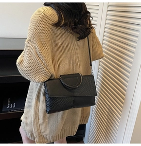 Detail of black crocodile texture handbag featuring a unique metal ring handle and shoulder strap
