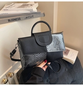 Detail of elegant black and grey snakeskin textured handbag with polished gold clasp