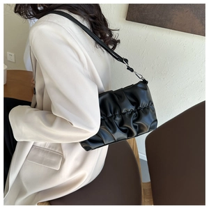 Close-up of black pleated cloud shoulder bag in glossy leather worn with a beige blazer