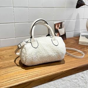 White lamb wool barrel pillow bag with leather straps on a wooden table for autumn winter
