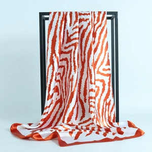 Elegant orange and white zebra print satin square scarf displayed on a modern black stand