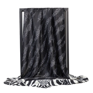 Detailed texture of black and white leopard print satin silk scarf draped on metal rack