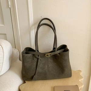 Deep olive green large tote bag with gold buckle on wooden base in a minimalist room