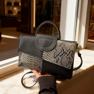 Elegant grey snake pattern and black leather patchwork handbag on marble surface