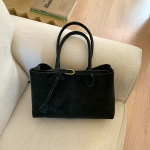 Large black suede tote bag with golden buckle and sleek leather handles on a chair