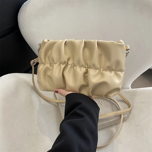 Minimalist beige pleated dumpling bag on a white sofa with adjustable shoulder strap
