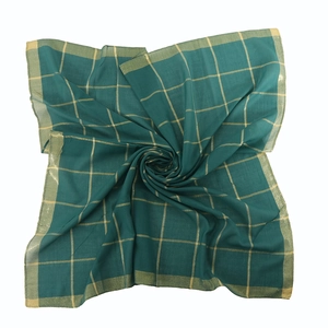 Detailed view of dark green silk scarf with gold grid pattern and stitched edges