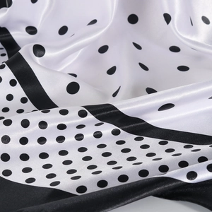 Détail d'un foulard en satin soyeux montrant la texture brillante et les pois noirs