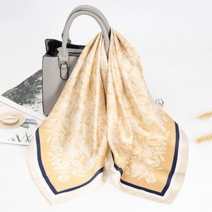 Elegant mustard yellow paisley silk square scarf tied to a leather handbag handle