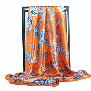 Golden phoenix paisley silk scarf in orange and blue displayed on a sleek black metal rack