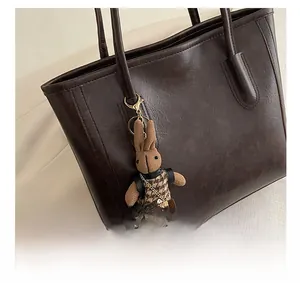 Nahaufnahme eines gestrickten Hasen-Anhängers mit Hahnentritt-Weste an brauner Ledertasche