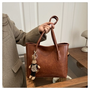 Braune Retro-Tote-Bag aus PU-Leder mit Hahnentritt-Hasenanhänger-Detail in der Hand