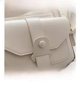 Detail view of cream leather shoulder bag showing the curved flap buckle and smooth texture