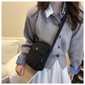 Detail of minimalist black nylon crossbody phone bag with round metal logo and strap