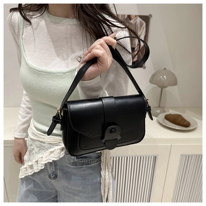 Close-up of minimalist black leather shoulder bag with gold hardware worn by model