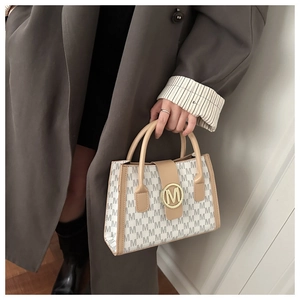 Detail of minimalist cream handbag with M-pattern and gold circular metallic buckle