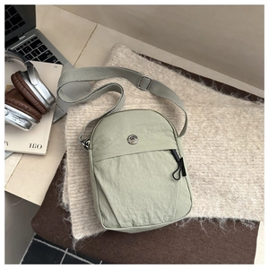 Detail of light green waterproof crossbody bag with metallic logo on beige knit background