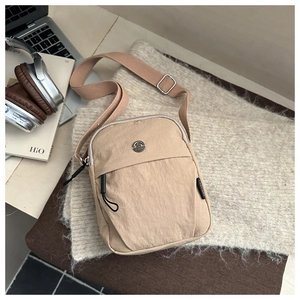 Detailed close-up of khaki nylon shoulder bag featuring a round metal logo and adjustable strap
