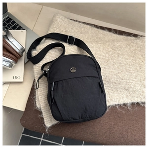 Detail of a black nylon crossbody bag with metal M logo and adjustable strap
